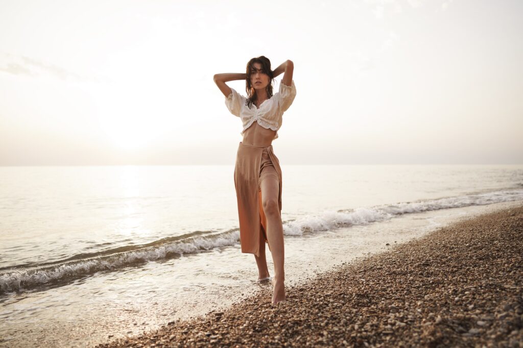 Lonely young woman walks on the seashore at sunset